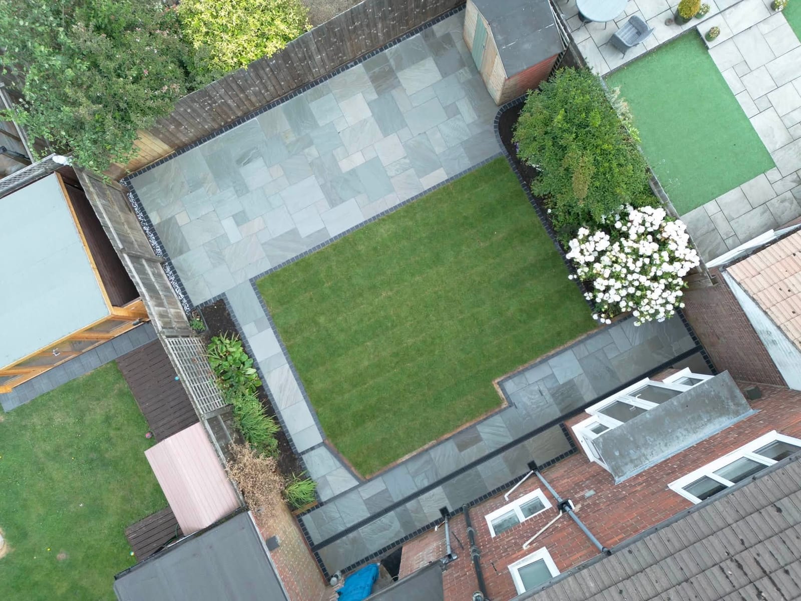 A drone view of a garden with a new grey porcelain patio, path and striped lawn