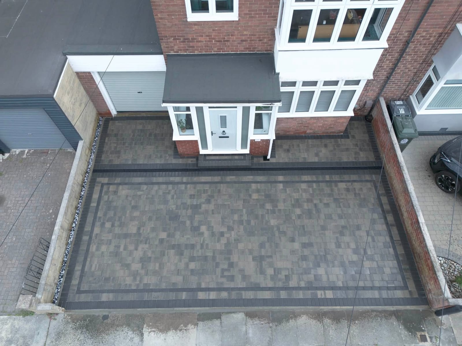 A drone view of a new grey block paved driveway in front of a semi-detached house